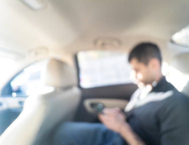 Adamın cep telefonuna dokunduğu ve arabanın içindeki koltukta oturduğu soyut bulanık arkaplan. Kişiyle birlikte bulanık araç
