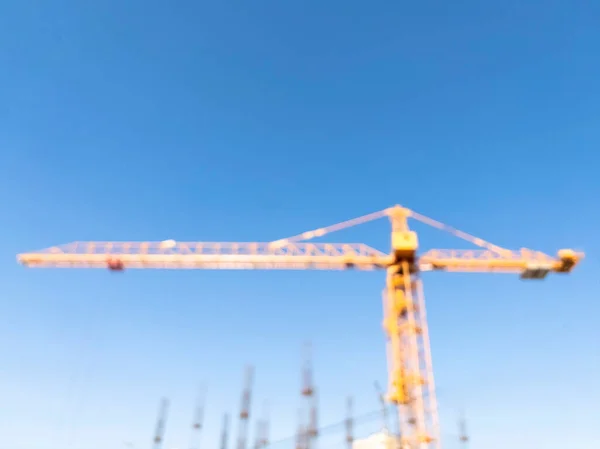 Blurred background with construction crane tower on blue sky. Crane and building working progress. Construction concept. Site. New buildings with a crane. Tower crane