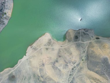 Dağ gölündeki hava manzarası. İnsansız hava aracı dağ vadisindeki su deposunu görüyor. Dağlık araziler arasında dağ gölünün pürüzsüz mavi yüzeyinden güzel bir manzara. Üst görünüm