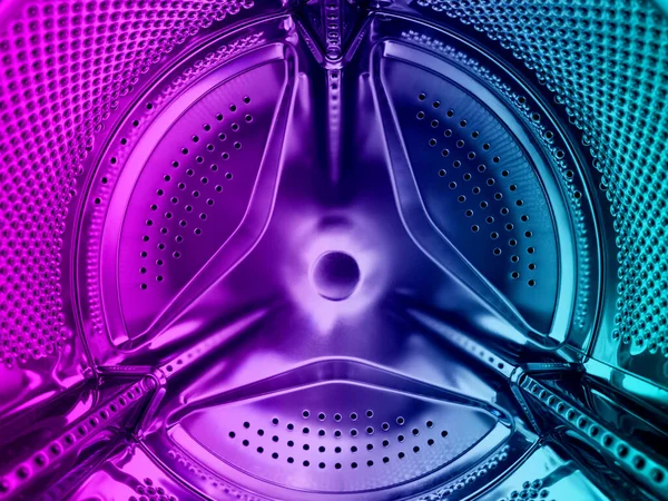 Washing machine drum close up. Washing machine background. Inside the washing machine. Metal washing machine drum in blue and pink tones. Perforated shiny metal