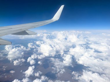 White wing from airplane window on sunny day. Great views of landscape. Aerial view of clouds through a plane window. Wing of airplane with blue sky and beauty clouds
