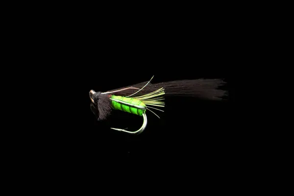 Macro shot colorful fishing fly isolated on a black background. Hand made fly fishing flies. Fluffy fly fishing hook isolated.
