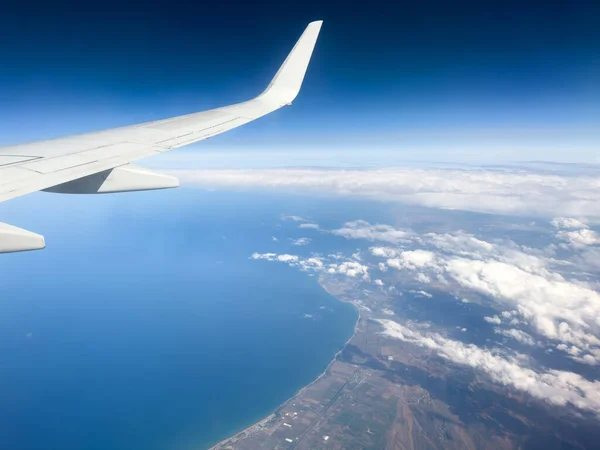Aerial view of ocean through a plane window. Wing of airplane with blue sky and beauty clouds over the ocean. Aerial sea view