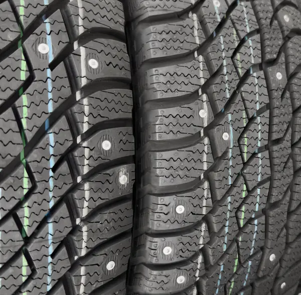 Winter studded tire. Winter car tires background. Tire stack background. Tyre protector close up. Square powerful spikes. Black studdable winter tyre profile.