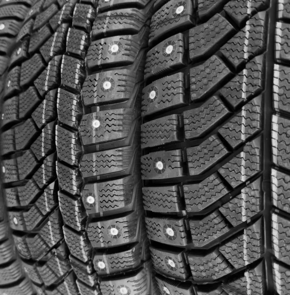 Winter studded tire. Winter car tires background. Tire stack background. Tyre protector close up. Square powerful spikes. Black studdable winter tyre profile. Car tires in a row