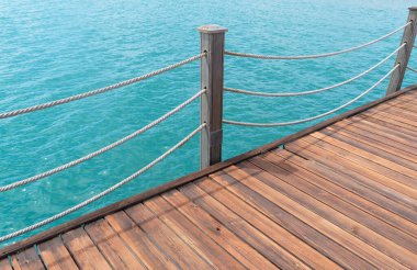 Sopalı ahşap iskele ve köpüklü deniz suyu olan halatlar. Mavi deniz zeminli ahşap iskele..