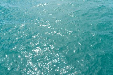 Mavi deniz suyu arka planı ve güneş yansımaları. Hava aracı görüntüsü. Dalgalar su yüzeyinde. Okyanus üzerinden uçmak. Havadan okyanus manzaralı. Denizin üstünde uç.