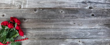 Kırmızı gül çiçekleri ve kırsal ahşap arka planda kalp şekilli bir kurdeleyle Sevgililer Günün kutlu olsun.