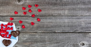 Sevgililer Günü karşılama konsepti zarflı, çikolatalı kurabiyeler ve ahşap arka planda küçük kırmızı kalpler.
