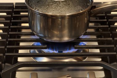 Modern Kitchen stove top cook with pan. Gas flame close up on a natural gas stove range burner with metal grill
