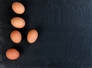 Organic brown chicken eggs on black stone background in flat lay view 
