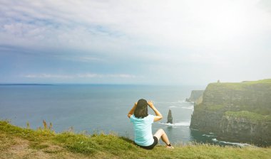 Woman looking into ocean and cliffs during a bright day in the summer 