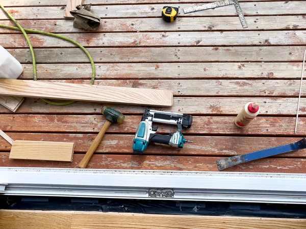 Interior home construction of wood floor being installed up to exterior door jam with carpenter tools on outside desk