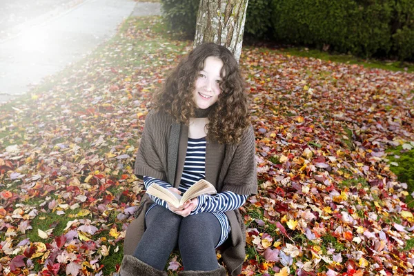 ティーン女の子屋外読書本中秋シーズンとともに庭と木で背景に光効果 — ストック写真
