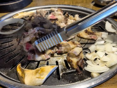 Çiğ, ince dilimlenmiş et ve soğanı ocakta hareket ettiren maşaları kapatın. 