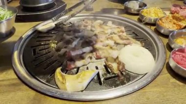 Çiğ, ince dilimlenmiş et ve soğanları doğal gaz ocağında hareket ettiren maşaları kapatın. 