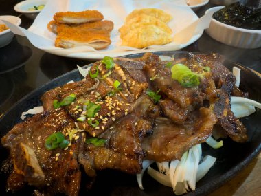 Kemiğin üzerine ince dilimlenmiş gevrek barbekü ve arka planda mezeler.  