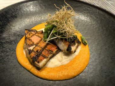 Domates sosunun üstünde ızgara somon balığı ve yakın planda doğranmış sebze. 