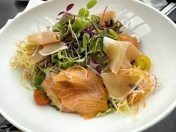 İnce dilimlenmiş biftekle taze salata ve beyaz tabakta balık.  