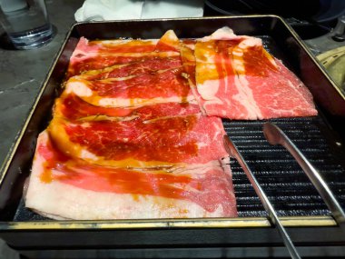 İnce dilimlenmiş çiğ eti Japon barbekü pişirme makinesinin yanına koy.  