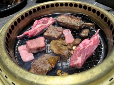 Biftek, domuz eti ve kuzu eti gibi çeşitli çiğ etleri Japon barbekü pişirme makinesine kapatın.  
