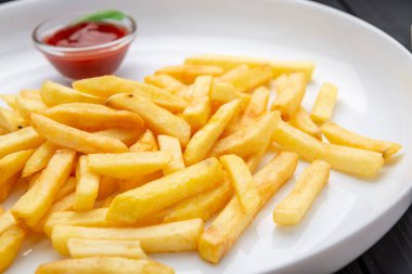 İştah açıcı meze. Beyaz tabakta ketçaplı patates kızartması. Siyah bir arkaplanda