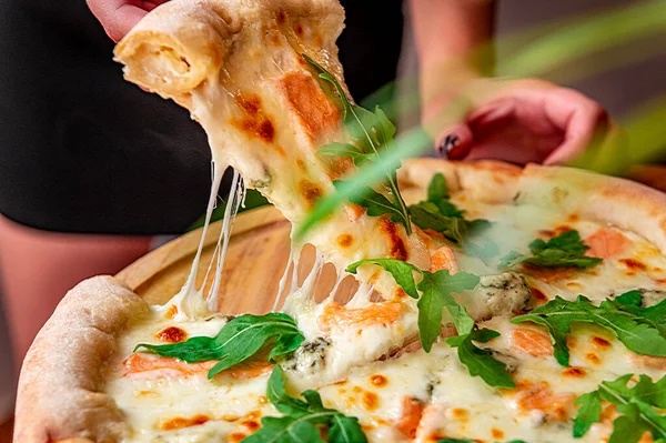 stock image Delicious hot pizza with salmon, arugula and different spices on wooden table ready to eat. Tasty and big pizza with different types of meat. Top view of big pizza