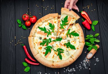 Somon, roka ve ahşap masada yenmeye hazır farklı baharatlarla nefis sıcak pizza. Lezzetli ve farklı et çeşitleriyle büyük pizza. Büyük pizzanın en üst görüntüsü