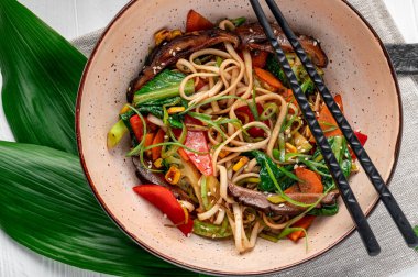 Udon stir fry noodles with beef meat and vegetables in a plate on white wooden background. Asian cuisine. Delicious and healthy food. Photo for the menu.