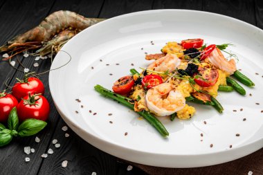 Omelet with shrimp, caviar and grilled tomatoes on a bed of asparagus beans and bacon. Serving food in a restaurant. Healthy food concept clipart