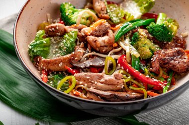 Udon stir fry noodles with pork meat and vegetables in a plate on white wooden background. Asian cuisine. Delicious and healthy food. Photo for the menu.