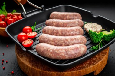 Summer food. Raw homemade sausages with vegetables on a grill pan.