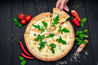 Somon, roka ve ahşap masada yenmeye hazır farklı baharatlarla nefis sıcak pizza. Lezzetli ve farklı et çeşitleriyle büyük pizza. Büyük pizzanın en üst görüntüsü