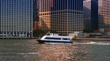New York, ABD, 4 Temmuz 2025: Modern motorlu tekne nehir kıyısında hareket ediyor. Sahildeki yüksek binaların ön cepheleri. New York, ABD.