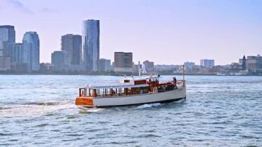 New York, ABD, 4 Temmuz 2025: New York, ABD 'de nehir kıyısında seyahat eden tekneyi takip ediyoruz. Arka planda sisli şehir silüeti.