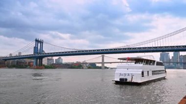 New York, ABD, 4 Temmuz 2025: New York 'ta East River' dan geçen büyük bir nehir teknesi. Bulutlu bir günde Manhattan Köprüsü ve Brooklyn Köprüsü alçak açılı..