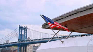 Teknede dalgalanan Amerikan bayrağı. Manhattan Köprüsü ve New York silueti.