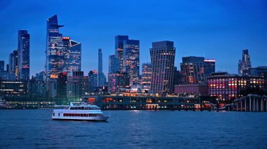 Turist teknesi alacakaranlıkta su kenarından geçiyor. New York 'un güzel şehir manzarası. Arka planda ışıklar açık..
