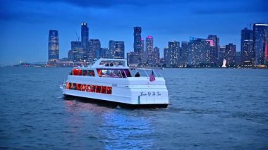 New York, ABD, 4 Temmuz 2025: Tatilciler alacakaranlıkta nehir teknesiyle seyahat ederler. Parlak New York 'un göz kamaştırıcı silueti..