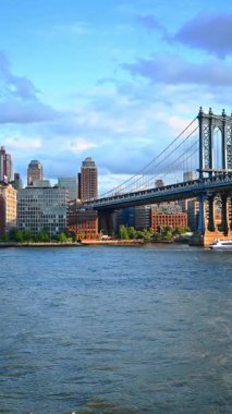 Nehir teknesi Manhattan Köprüsü 'nün altından geçiyor. Doğu Nehri 'nin su manzarasından köprüyü ve New York binalarını izleyin. Dikey video.