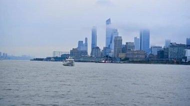 Modern beyaz nehir teknesi nehrin su manzarası ile yaklaşıyor. New York 'un gökdelenli silueti sislerin arasında yarı gizlidir..