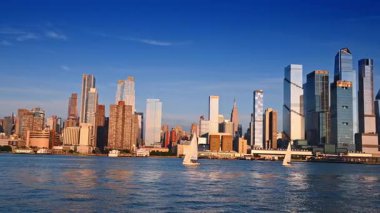 New York, ABD, 8 Temmuz 2025: İki yelkenli nehir manzarasından geçiyor. New York, ABD 'de modern yoğunlukta inşa edilmiş güneşli gökyüzü.