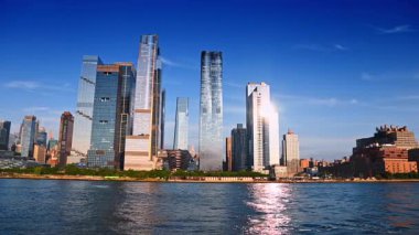 New York, ABD, 8 Temmuz 2025: Parlak güneş yüksek binaların cephelerine yansıyor. Nehirden ABD 'nin New York limanındaki binaların alçak açılı görüntüsü.