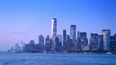 Pencerelerinde birden fazla ışık olan New York silueti. Alacakaranlıkta nehir manzarasından şehir manzarasına bak.