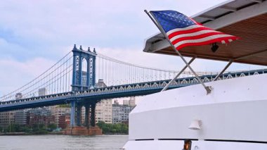 Rüzgarda dalgalanan bir Amerikan bayrağıyla nehir teknesinden görüntüler. Manhattan Köprüsü 'nün arka planında alçak açılı görüş.