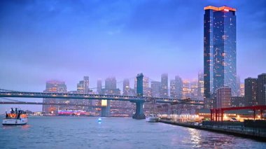 New York 'un canlı akşam silueti. Şehir ışıkları New York 'ta alacakaranlıkta parlıyor, nehir manzarası ve canlı mahalleleri birbirine bağlayan bir köprü var..