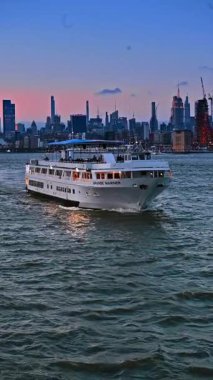 New York, ABD, 8 Temmuz 2025: New York Limanı 'nda gün batımı gezisi. Bir yolcu gemisi alacakaranlıkta New York Limanı 'ndan geçiyor, şehrin ufuk çizgisi günbatımı renkleriyle aydınlanıyor..