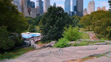 New York, ABD, 8 Temmuz 2025: New York 'taki Central Park' ı keşfetmek. Ziyaretçiler Central Park 'taki doğa ve aktivitelerin keyfini çıkarırken, gökdelenler güneşli arka planda yükseliyor..