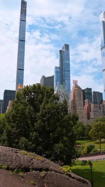 New York, ABD, 8 Temmuz 2025: Gökdelenli park manzarası. Ziyaretçiler, New York 'un parlak bir gününde gökdelenlerle Central Park' ın yeşilliğinin keyfini çıkarıyorlar..