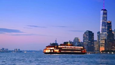 Büyük parlak nehir botu alacakaranlıkta nehir manzarası boyunca seyahat eder. Manhattan, New York 'un yüksek gökdelenli silueti.